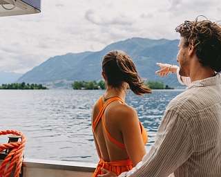 Paar auf einem Boot zeigt in Richtung der Brissago Inseln auf dem Lago Maggiore – ein beliebter Tagesausflug in der Region rund um das Sunstar Hotel Brissago.