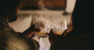 Le plaisir du whisky dans l'ambiance Deux personnes tiennent dans leurs mains des verres à whisky décorés d'où s'élève une légère vapeur. La scène est baignée d'une lumière chaude et tamisée.