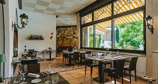 Salle à manger baignée de lumière avec vue sur le jardin Vaste espace restaurant avec de hautes fenêtres donnant sur une terrasse verdoyante et luxuriante. Les tables sont élégamment dressées pour les invités.