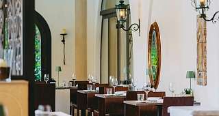 Ambiance méditerranéenne au restaurant Vue de la lumineuse salle de restaurant avec ses tables en bois recouvertes, ses lampes décoratives murales et son miroir ovale à l'hôtel Sunstar Brissago
