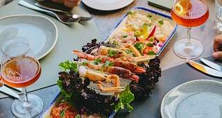 Assiette de hors-d'œuvre de la mer Un plat rectangulaire avec divers fruits de mer et salades. À côté, il y a des assiettes, des couverts et des verres avec une boisson rougeâtre.