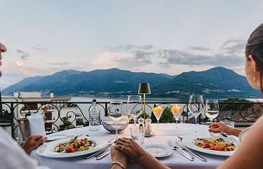 Couple attablé lors d'un élégant dîner aux chandelles sur la terrasse du Sunstar Hotel Brissago, entouré de verres de vin et de salades fraîches avec vue sur le lac dans la lumière du soir.