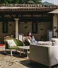 A woman sits smiling in a green armchair in the courtyard of the Sunstar Hotel Brissago. The lounge furniture is brightly coloured and surrounded by sunshine.