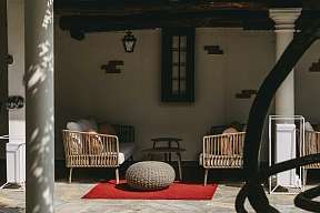 A covered corner in the inner courtyard with white columns, wooden beams and cosy rattan armchairs. A red carpet and a stone floor emphasise the Mediterranean flair