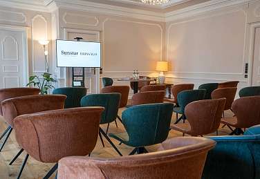 Heller Seminarraum im Sunstar Hotel Brissago mit Theaterbestuhlung, modernem Präsentationsbildschirm und stilvollen Lounge-Sesseln in Braun und Petrol