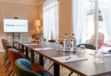 Bright meeting room at Sunstar Hotel Brissago with boardroom-style seating, presentation screen, water glasses and view of the private outdoor area