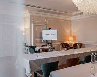 Eleganter Veranstaltungsraum im Sunstar Hotel Brissago mit Schulform-Bestuhlung, weissen Tischdecken, Präsentationsbildschirm und Kristallleuchter