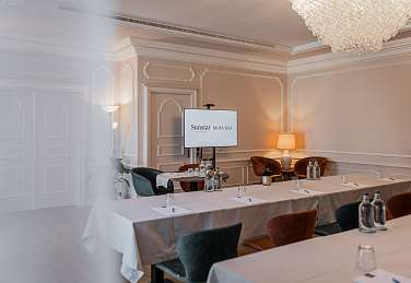 Eleganter Seminarraum im Sunstar Hotel Brissago mit Schulform-Bestuhlung, Präsentationsbildschirm, Kristallleuchter und warmem Ambiente