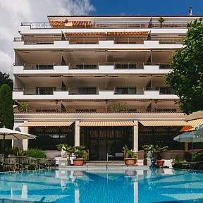 Piscina esterna soleggiata con lettini e ombrelloni davanti al Sunstar Hotel Brissago