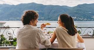 Commencez la journée ensemble Un couple est assis joyeusement à la table du petit-déjeuner sur le balcon. Il tient une tasse de café tandis qu'elle rit et savoure son repas.
