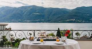 Petit-déjeuner avec vue panoramique sur le lac Majeur Une table dressée avec des assiettes, des verres à jus et un bouquet de fleurs, directement au-dessus du lac avec vue sur les montagnes environnantes